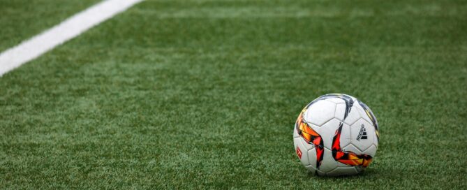A vibrant soccer ball resting on a pristine grass field beside a white sideline.